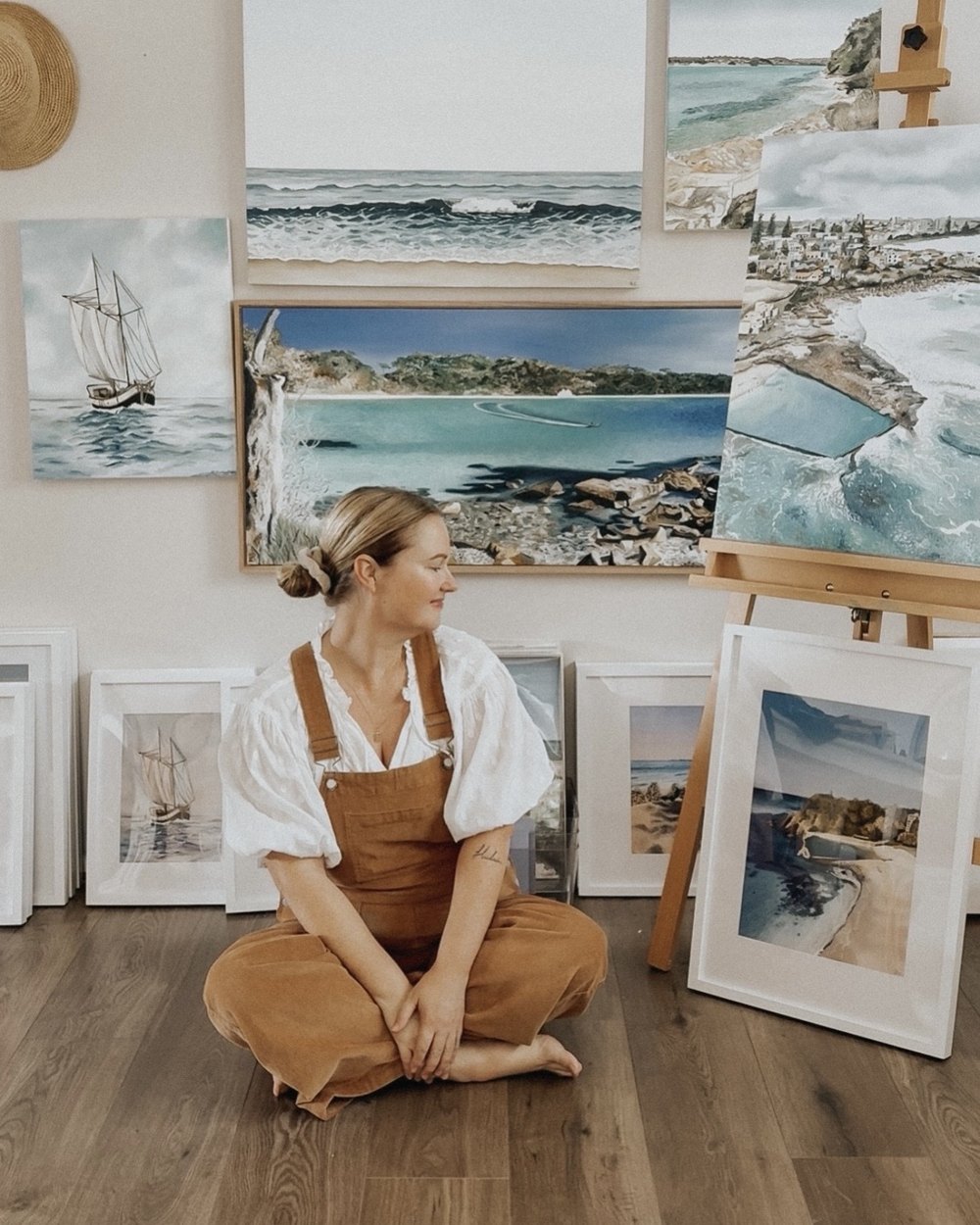 Bec Callaghan sitting on the floor of her home studio in Helensburgh, surrounded by her coastal paintings